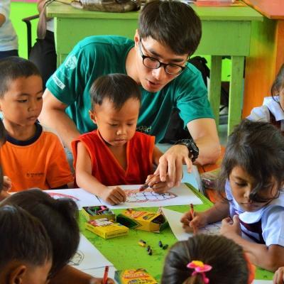 A Childcare volunteer helps a group of young children with a colouring excerise at his Childcare Project in the Philippines. A Projects Abroad volunteer working with children in the Philippines sits with a group of kindergarten children in a classroom during his Childcare Project.